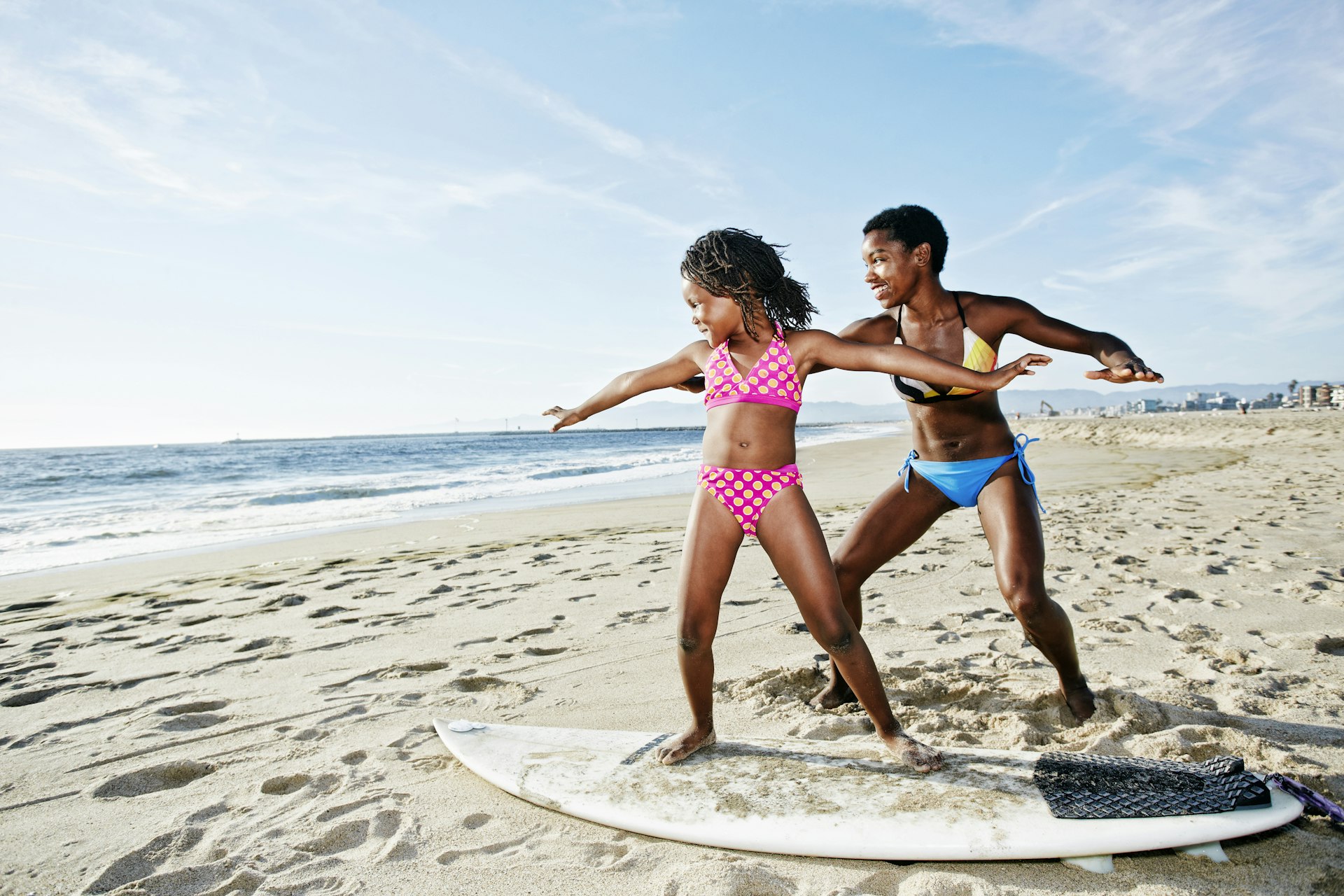 Black mother teaching daughter to surf on beach